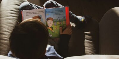 a little boy sitting on a couch reading a book